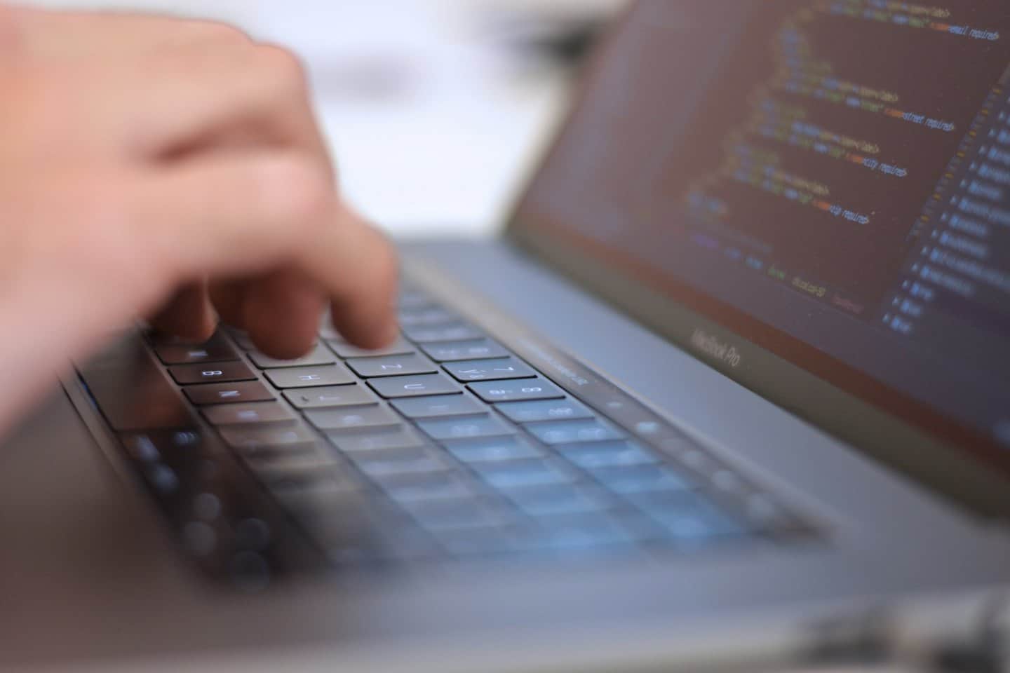 Manos escribiendo código de programación en el teclado de un portátil.
